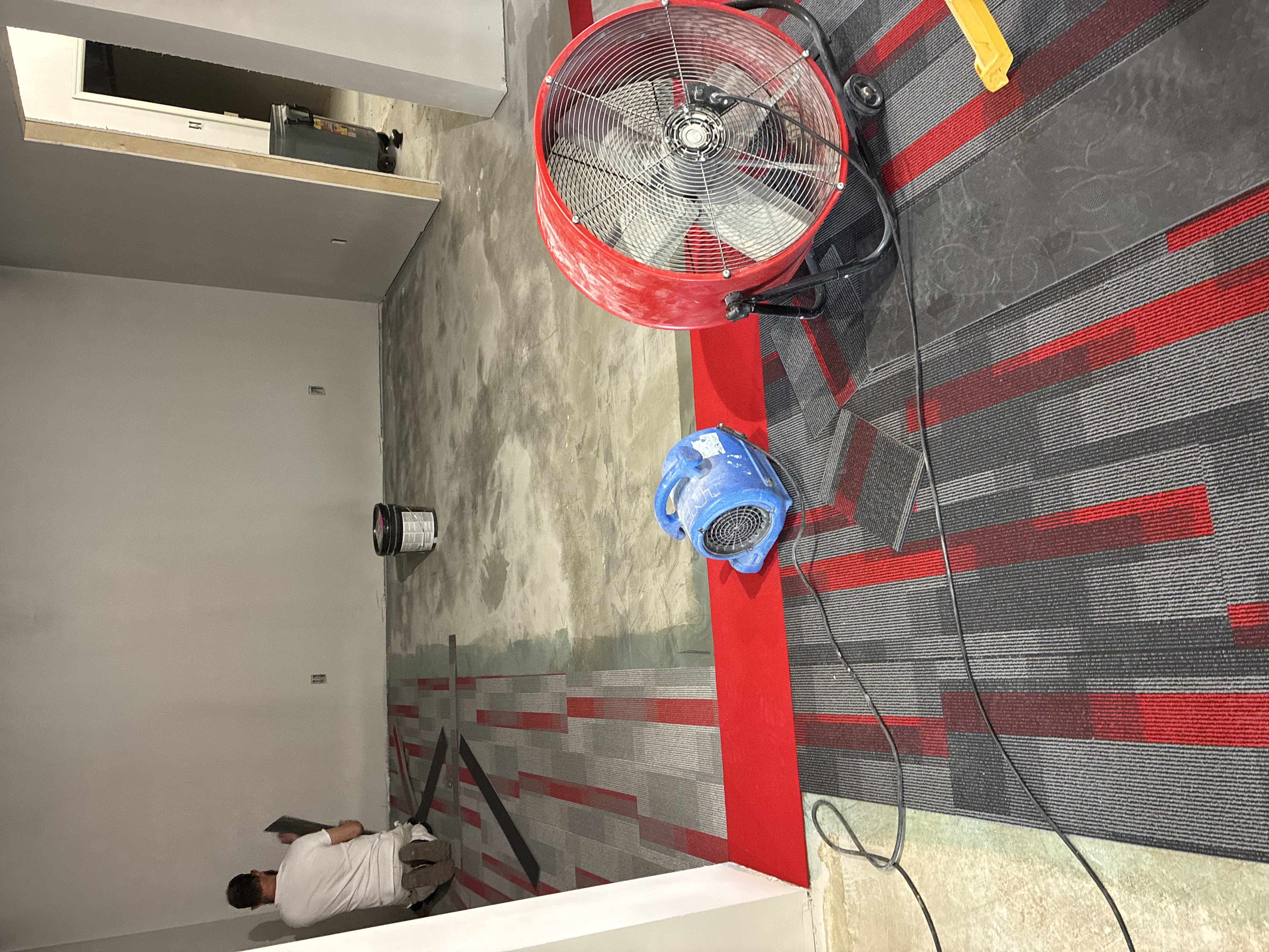 Commercial carpet tile installation crew with adhesive and air movers on concrete