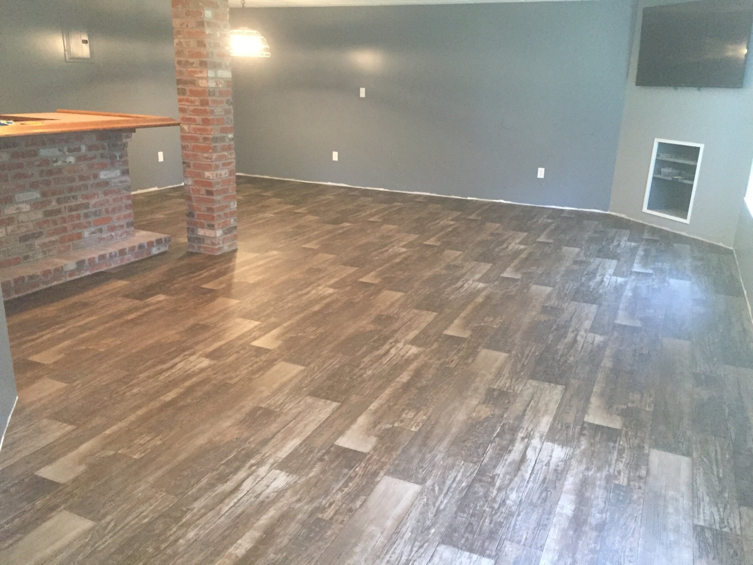 Wood-look sheet vinyl flooring in basement living room with brick pillar