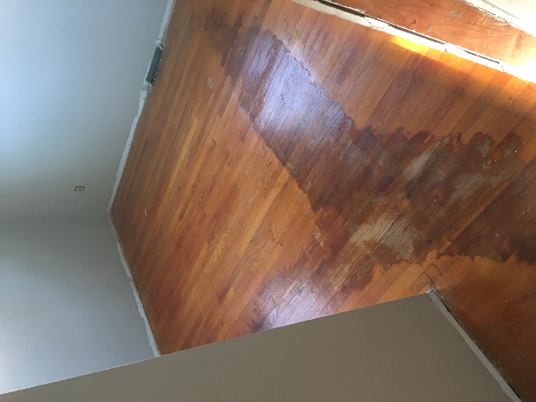 Damaged hardwood floor before refinishing - room with dark water stains and worn finish
