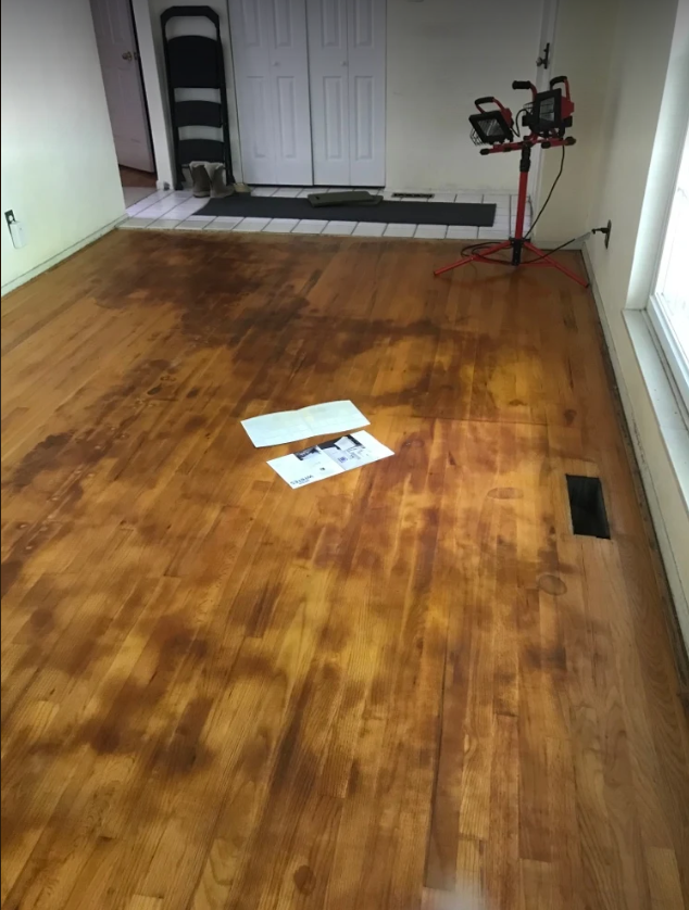Oak hardwood floor with deep dark water stains and damaged finish before refinishing